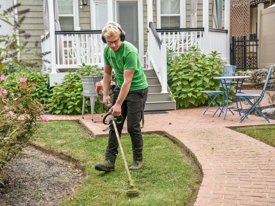 A landscaper edging a lawn beside a front walkway